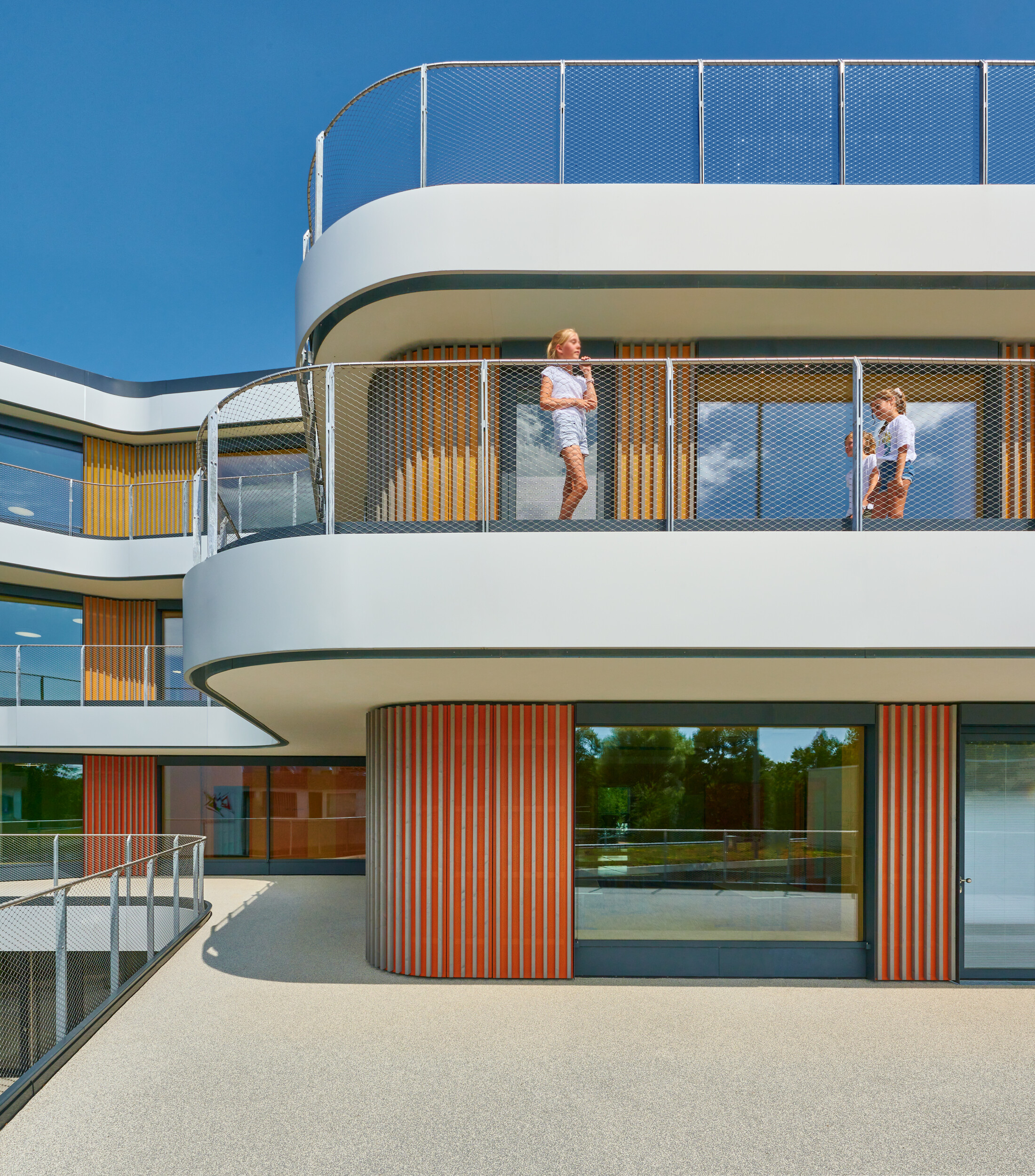 Project by Behnisch Architekturbuero, Gotthard-Müller-School Bernhausen. Two children stand on a curved balcony of the building with glass railing and colorful vertical facade elements.