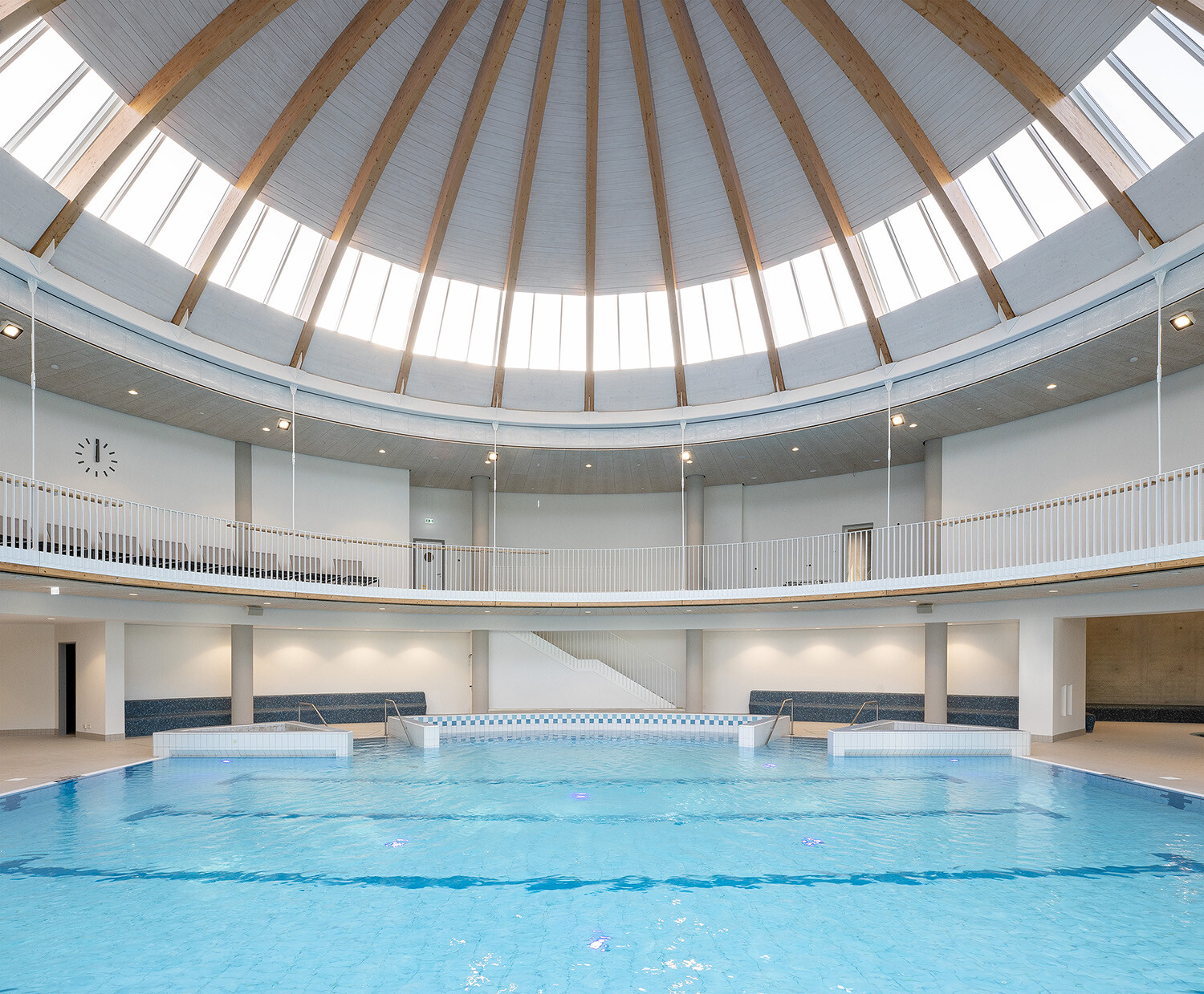 Project by Behnisch Architekturbuero, Wunnebad Winnenden. Indoor circular pool hall with central pool, surrounding gallery, and a skylit domed ceiling supported by wooden beams.
