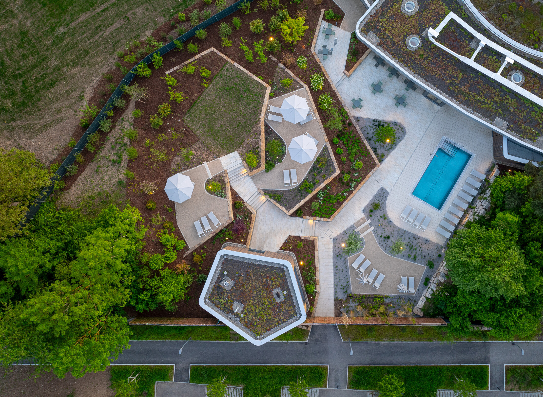 Project by Behnisch Architekturbuero, Wunnebad Winnenden. Aerial view of the building and its exterior. The outdoor pool of the spa area and the terraced seating and lounging areas are visible. The landscaping of the exterior and roofs is also visible.